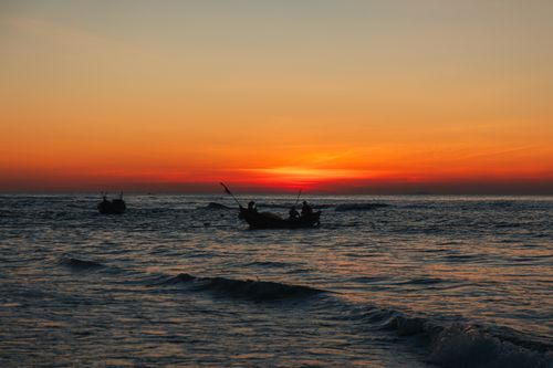 Free Silhouetted fishing boats during a vibrant sunset over the ocean in Quảng Trị, Vietnam. Stock Photo