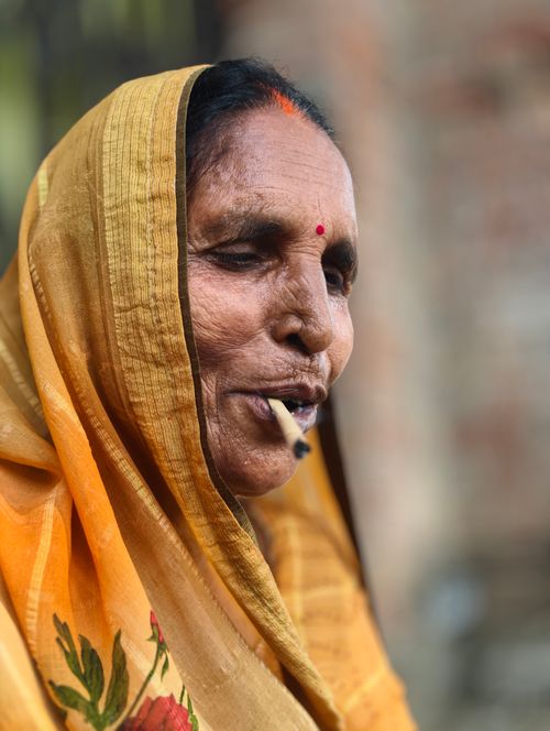Free Portrait of an elderly woman wearing a sari, smoking a pipe, displaying cultural attire. Stock Photo