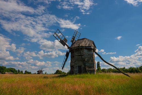 Free Old wooden windmill in a vast field under a vibrant blue sky with clouds. Stock Photo