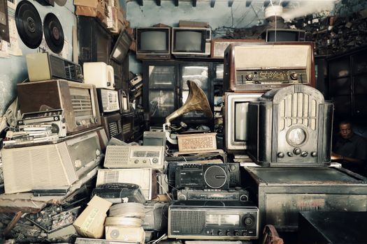 An array of vintage electronics, radios, and a gramophone in an antique shop with a nostalgic atmosphere.