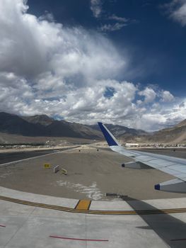 View from airplane window of Leh with dramatic skies and distant mountains.