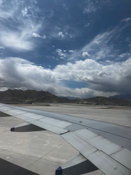 Wing view of an airplane over the stunning landscape of Leh, showcasing dramatic clouds and mountains.