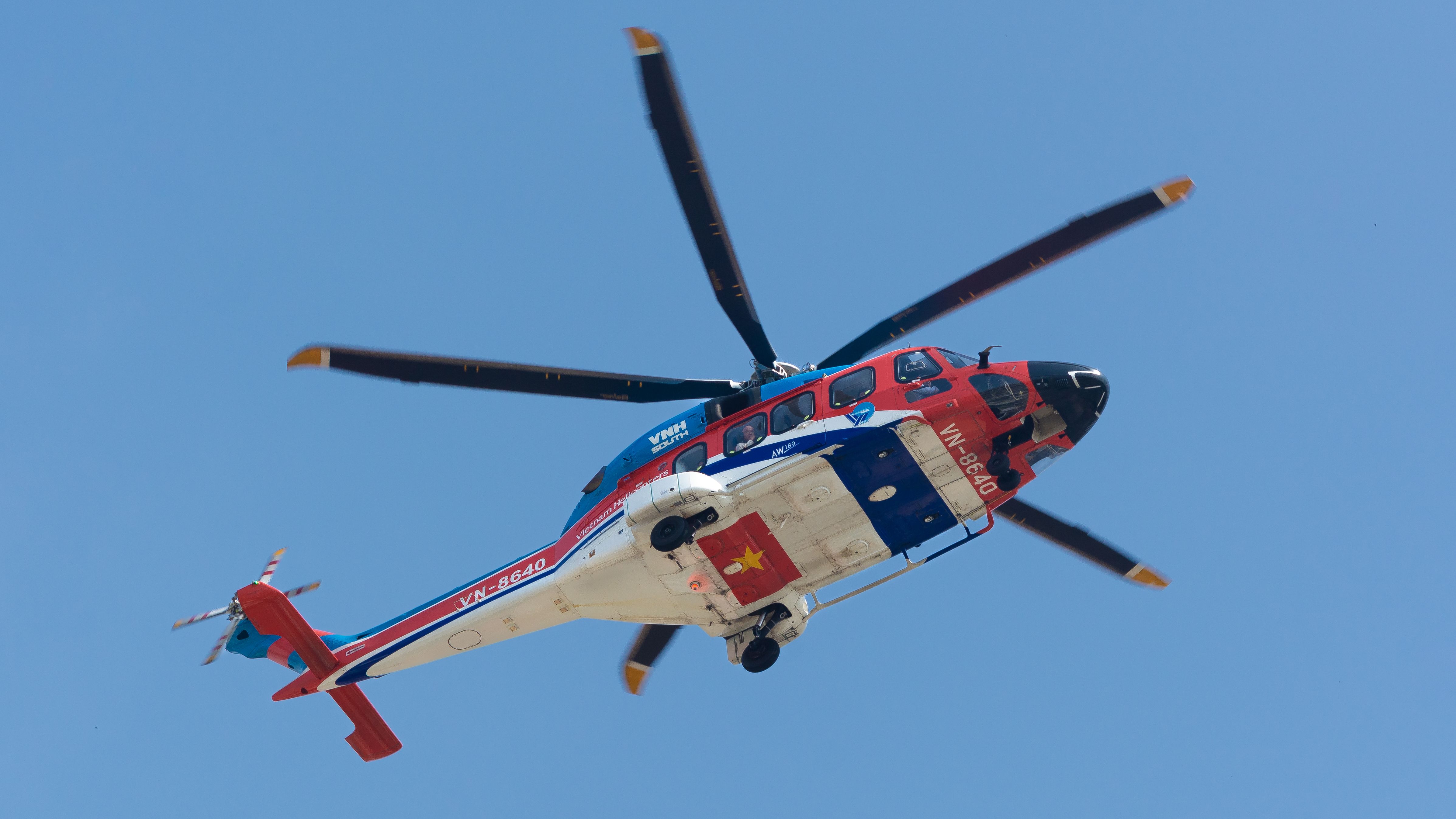 A red and blue helicopter in flight against a clear blue sky, showcasing its vibrant colors and design.