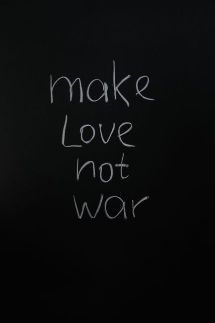 Vertical shot of 'make love not war' handwritten on a chalkboard, promoting peace.