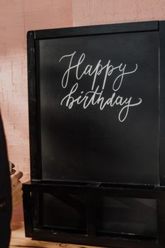 A chalkboard featuring artistic hand lettering of 'Happy Birthday' against a cozy indoor setting.