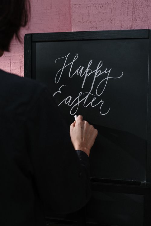Free A person writes 'Happy Easter' using chalk on a blackboard indoors. Stock Photo