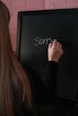 Woman in Black Long Sleeve Shirt Writing on the Chalkboard