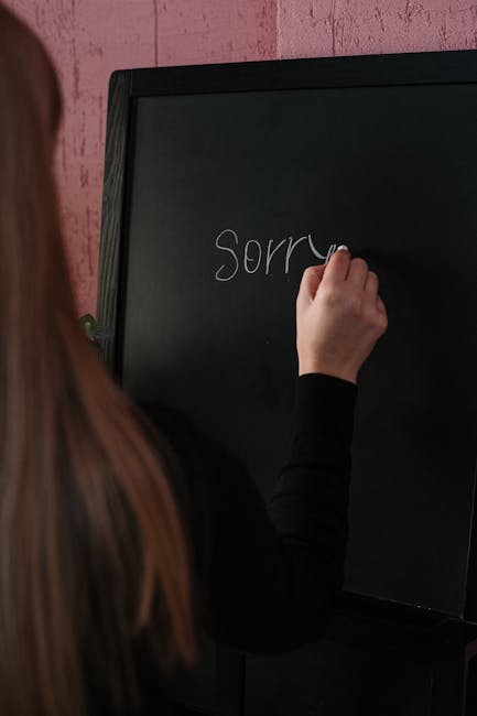 Side view of a person writing 'Sorry' on a blackboard indoors, conveying an apology.