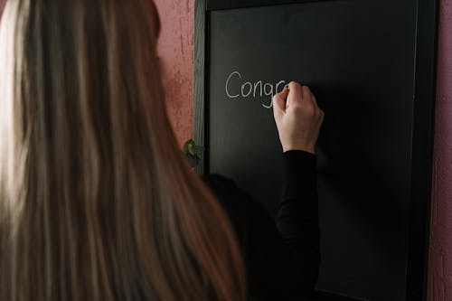 Woman in Black Long Sleeve Shirt Writing on Blackboard