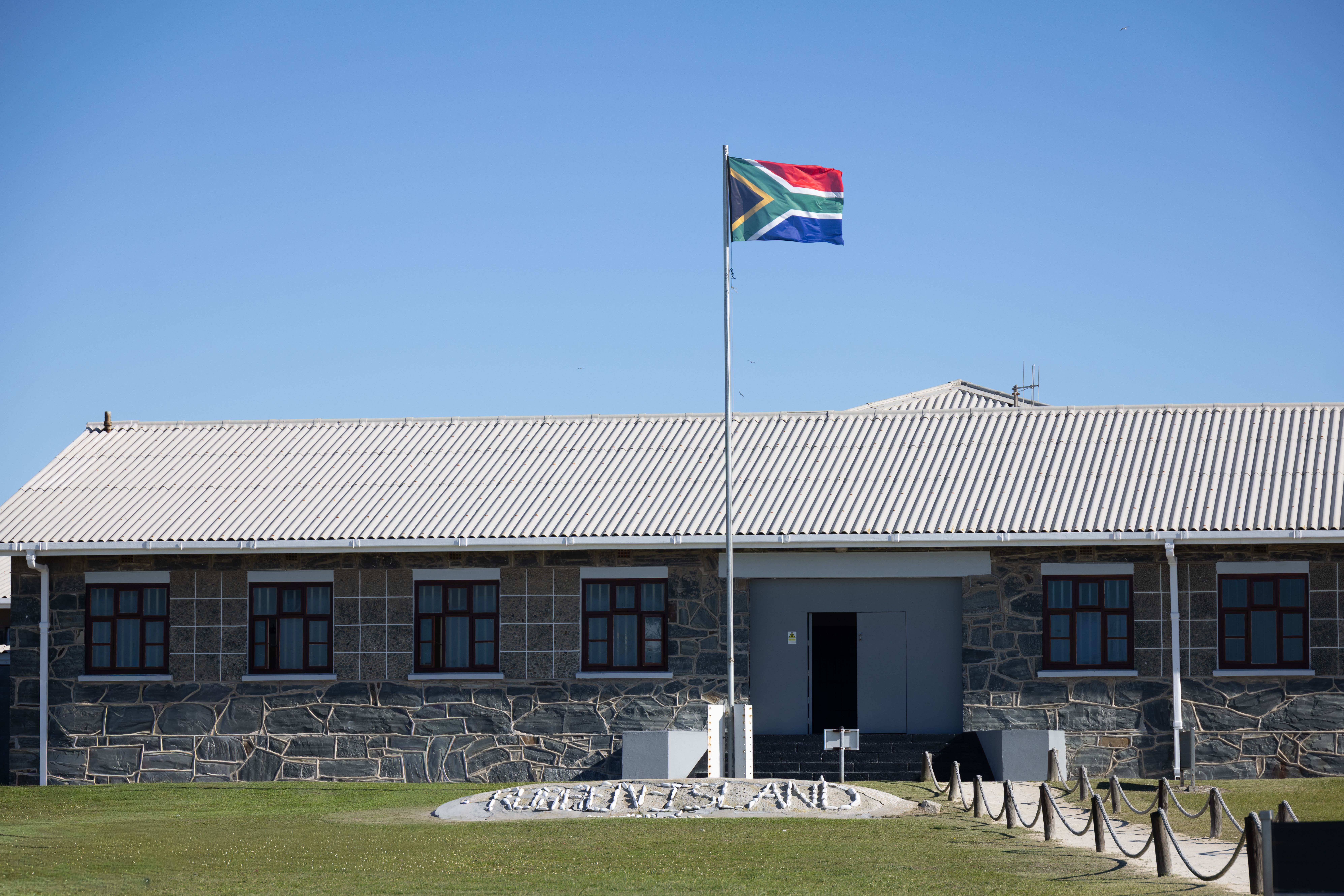 Robben Island Museum building with South African flag under clear blue sky.