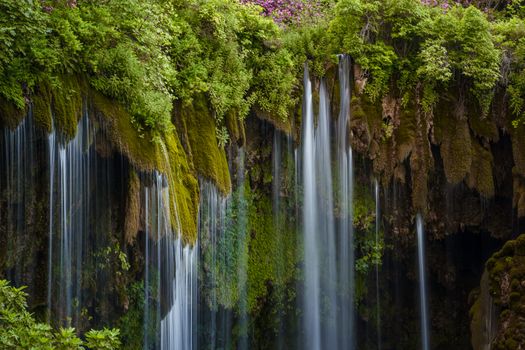 Breathtaking view of a powerful waterfall cascading over mossy rocks in Mersin, Türkiye, surrounded by vibrant spring greenery.
