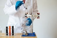Crop of unrecognizable scientist wearing lab coat and gloves and inserting pipette into empty flask mounted on ring stand while working in laboratory