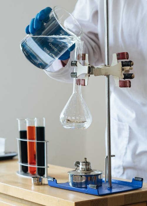 бесплатная Химик наливает прозрачную жидкость в хрупкую стеклянную посуду в научном центре Стоковое фото