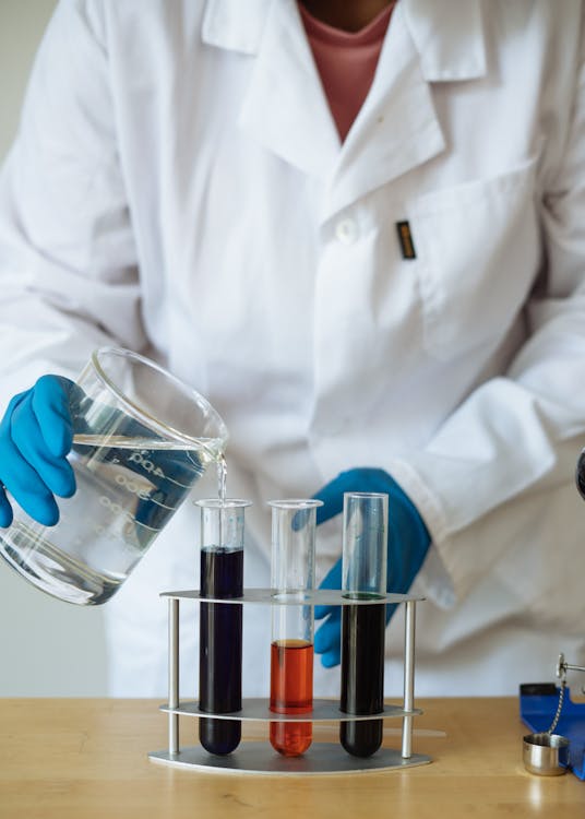 Free Crop of faceless researcher in uniform checking chemical reaction by pouring transparent liquid to test tubes with colored mixtures Stock Photo