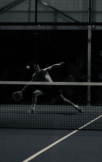 Black and white image of a padel player hitting the ball during a night match.