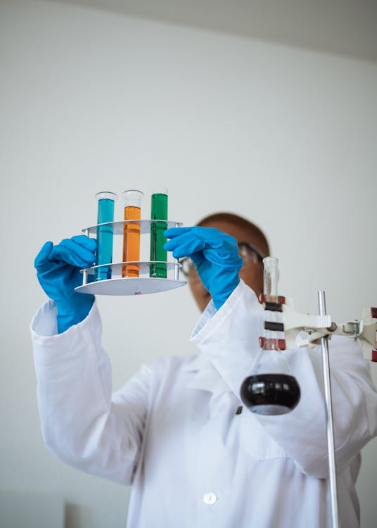 Unrecognizable African American chemist wearing uniform and analyzing chemical reaction while holding stand with test tubes in hands in modern lab