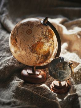 Two vintage globes rest on fabric, highlighting antique cartography in warm, natural light.