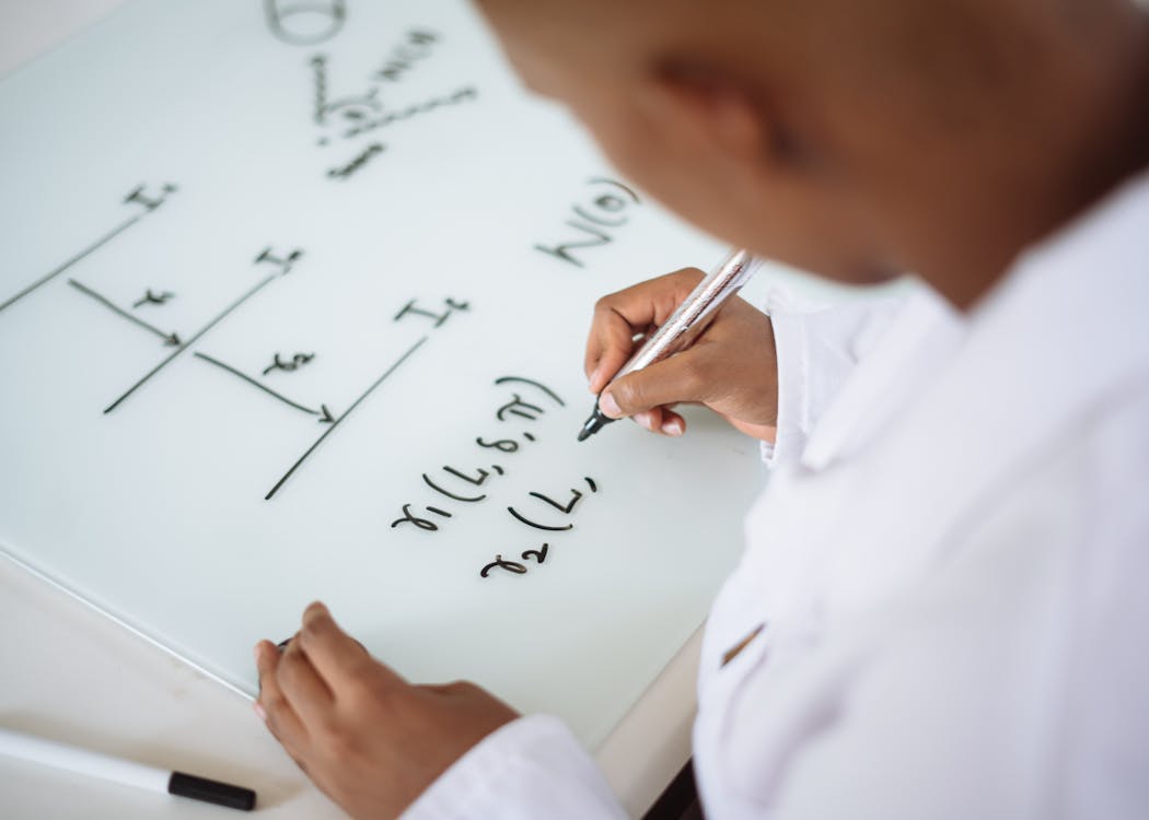 Free From above anonymous ethnic student wearing uniform and solving problem in chemistry while writing formula on white table in lab Stock Photo