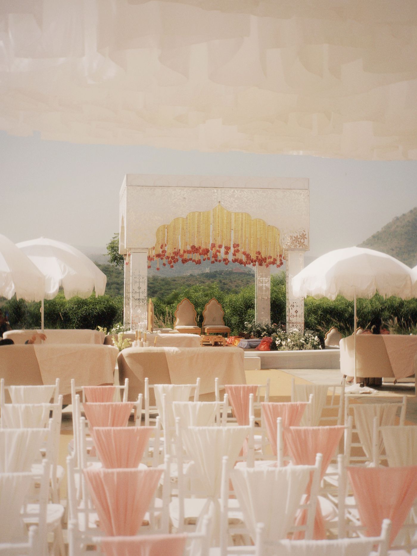 White jaali mandap and blush chiavari seating open to the hills — representative image