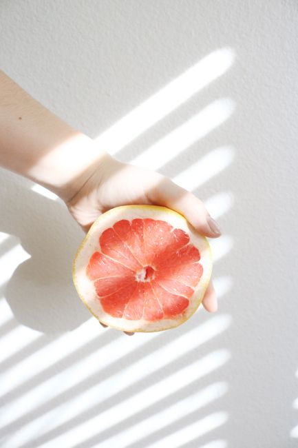 Bright close-up of a grapefruit slice held by a hand against a light background.