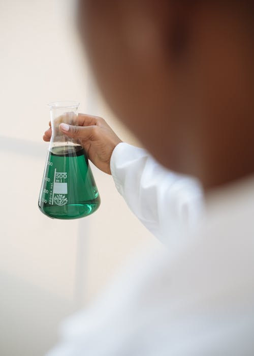 Person in White Lab Gown Holding Clear Glass Container