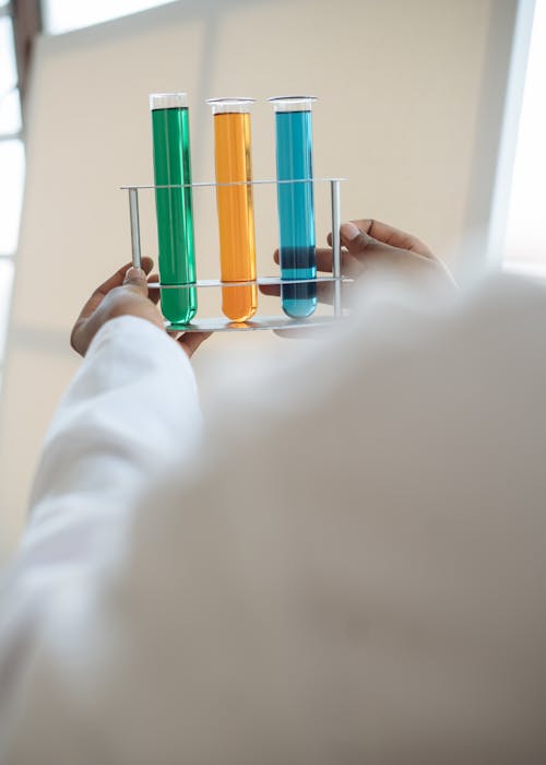 Free From above of unrecognizable ethnic scientist in uniform holding in hands stand with different reagents in test tubes while waiting for chemical reaction during test in lab Stock Photo