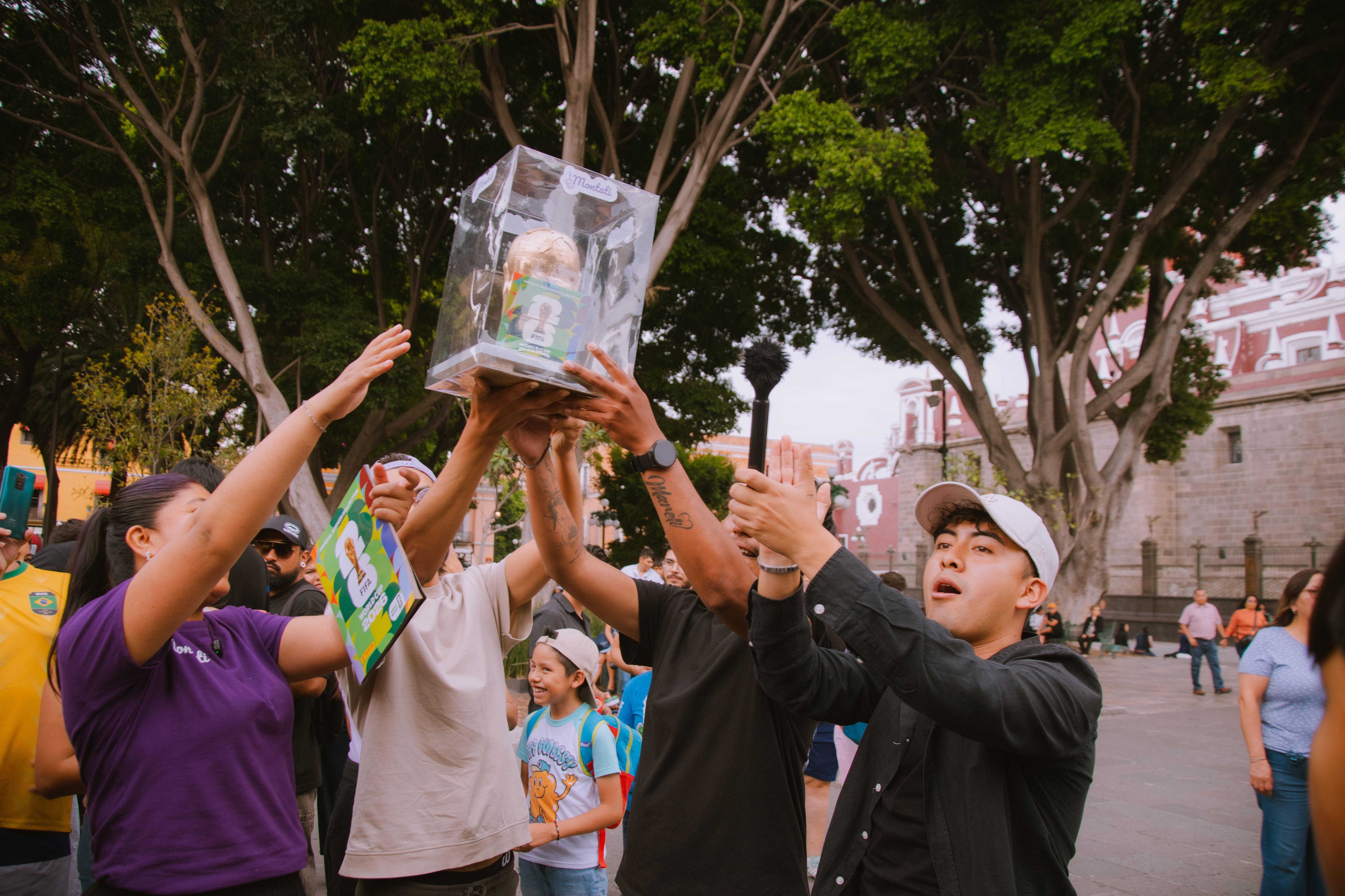 A diverse group of people celebrating together outdoors, holding a trophy.