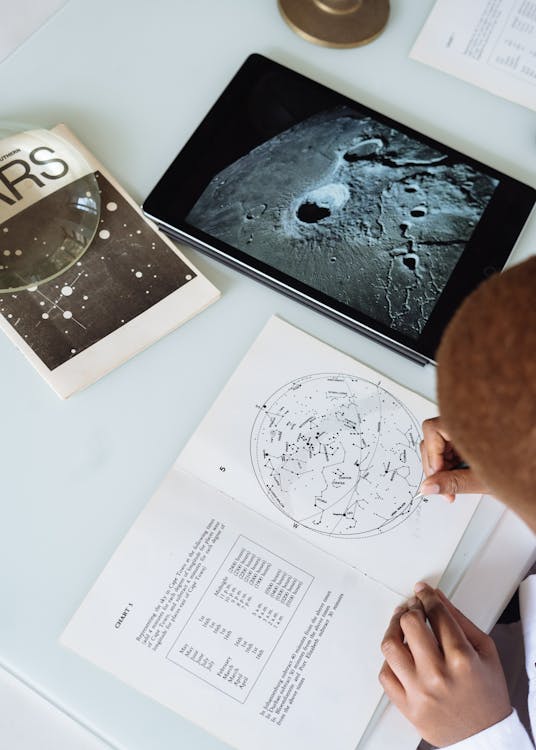 Free Crop of  faceless astronomer in uniform modifying astronomical map while sitting at table with tablet and educational materials conducting research at science center Stock Photo