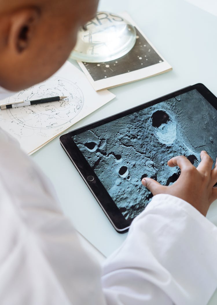 Crop Astrophysicist Exploring Surface Of Moon While Using Tablet In University