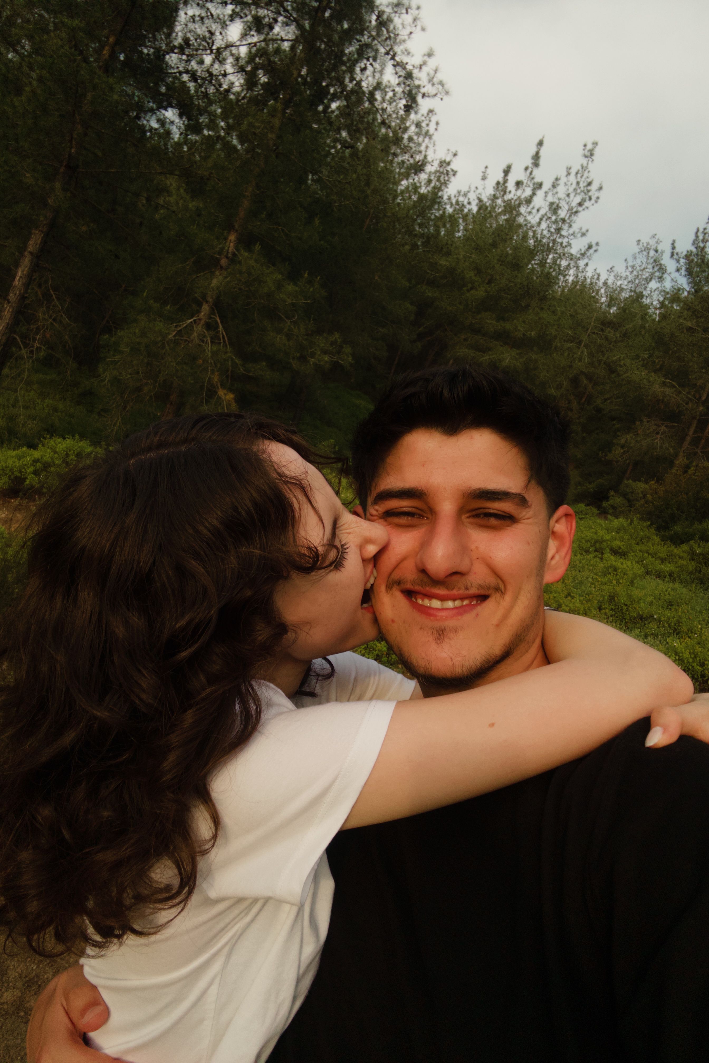 Joyful couple shares a loving embrace against a lush forest backdrop on a sunny day.