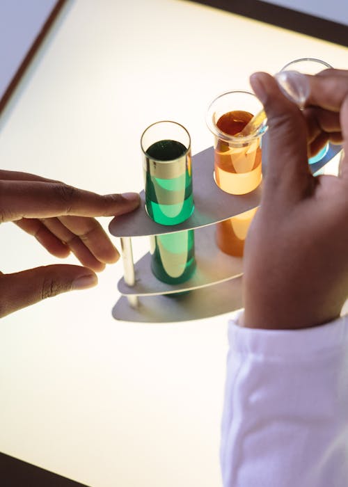 Crop laboratory technician in white uniform using pipette for taking sample from test tube during biochemical experiment in researching center