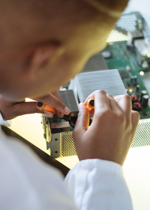 Free Crop of ethnic system administrator in uniform using screwdrivers and checking motherboard on electronic equipment during work in repair department Stock Photo