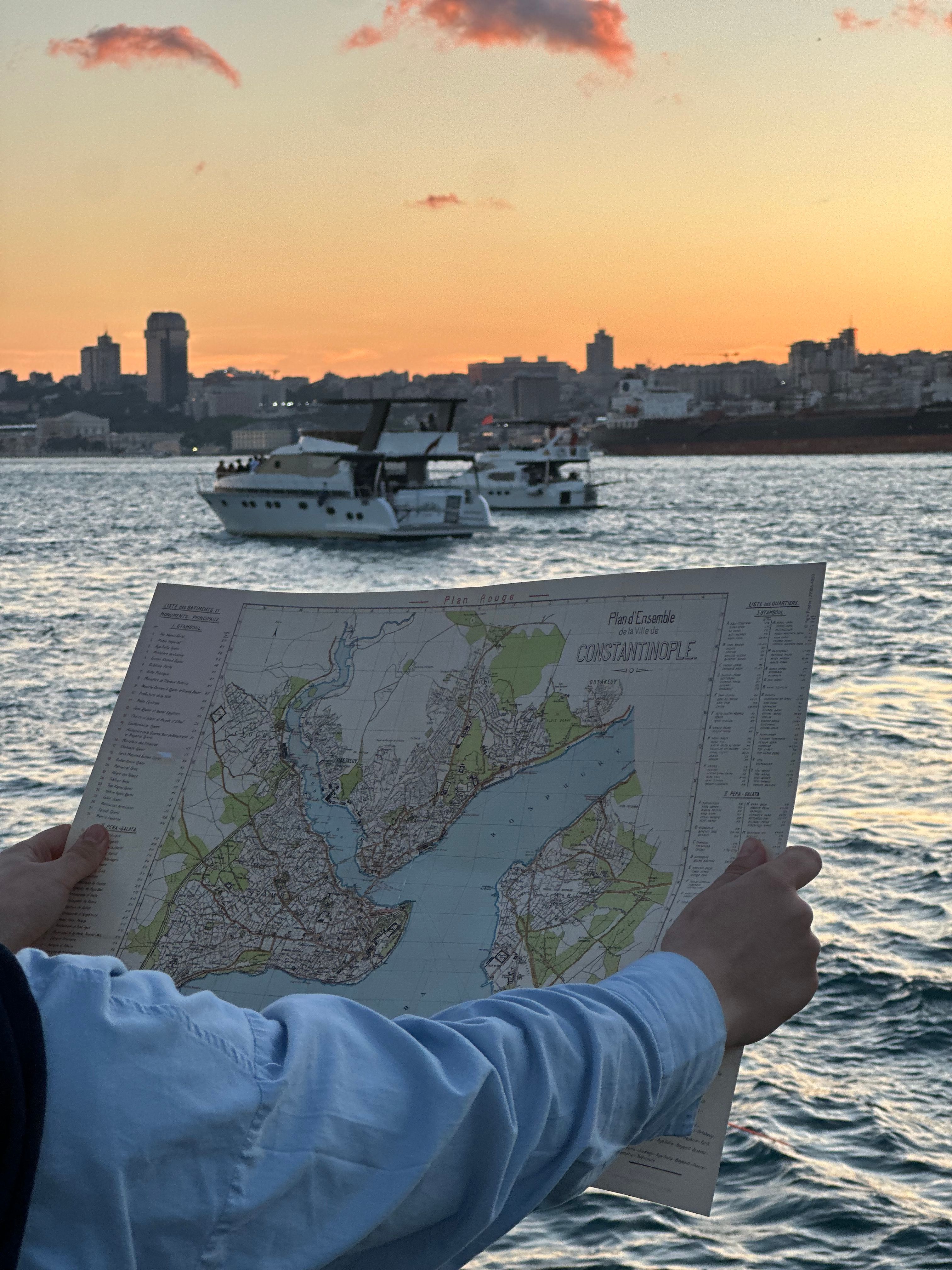 Person holding a map of Constantinople with boats and a city skyline at sunset on the Bosphorus.