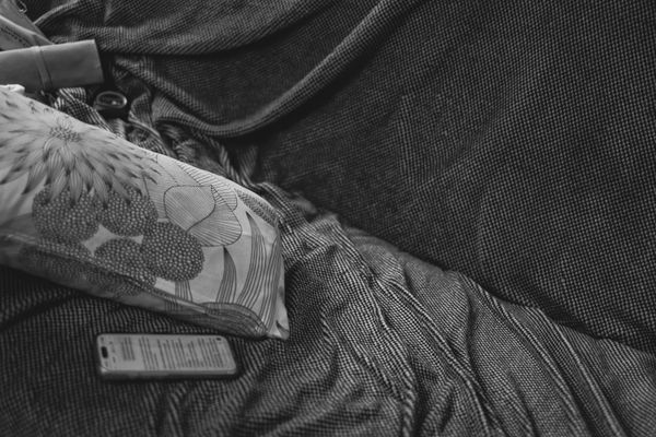 Nature morte en noir et blanc d'un coussin fleuri et d'un téléphone sur un lit défait