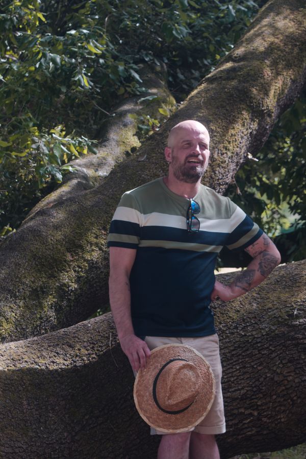 Portrait détendu d'un homme au chapeau de paille appuyé contre une branche