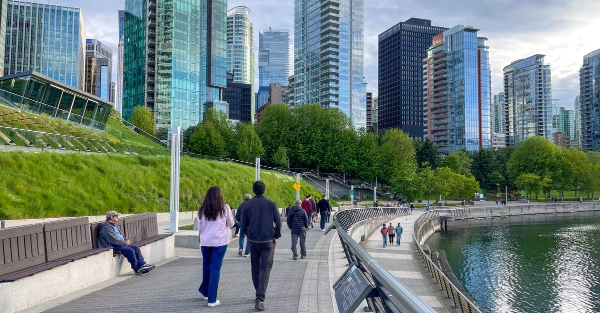 People strolling along Vancouver's scenic waterfront with skyline views of modern glass buildings.