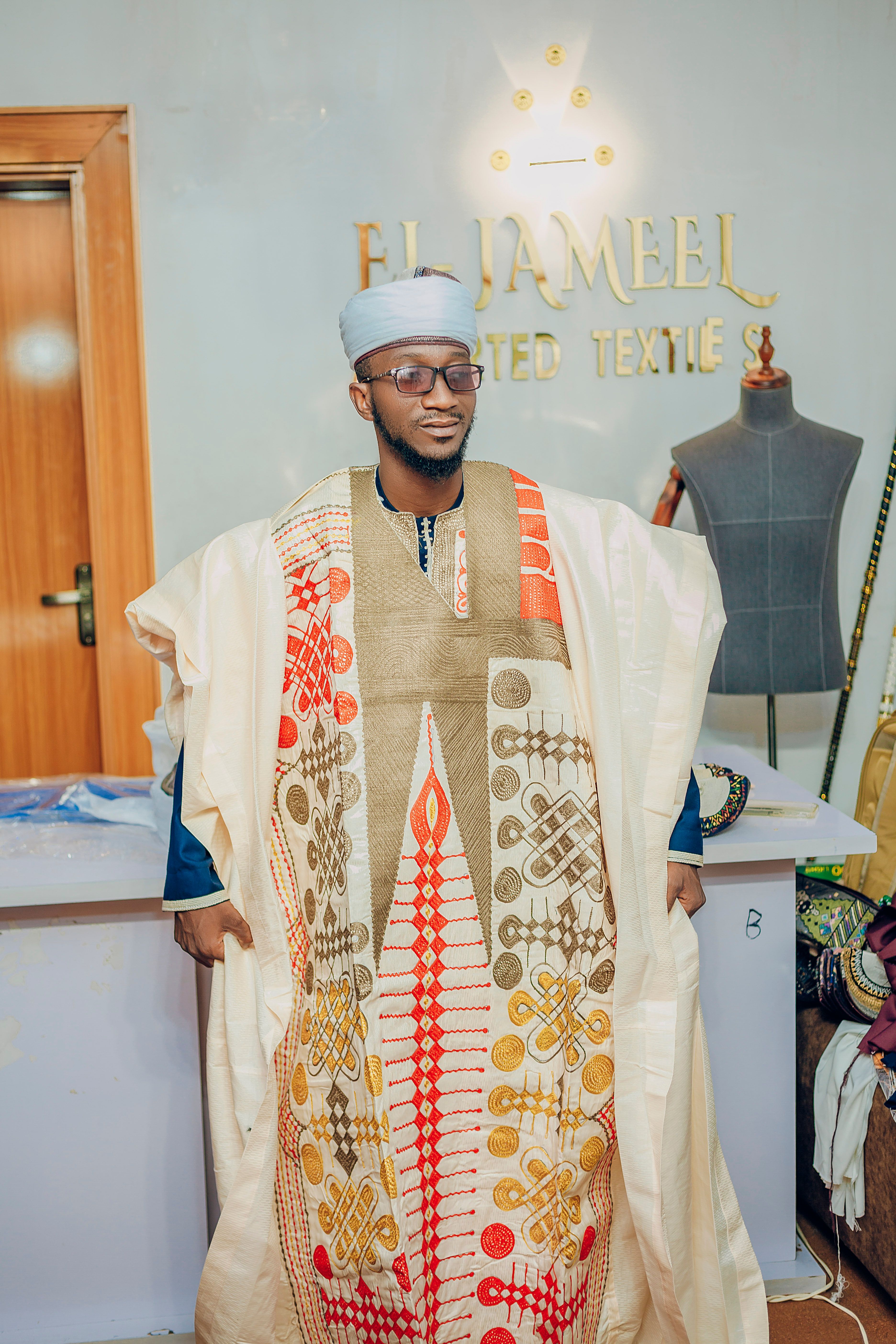 Man wearing embroidered traditional attire in a vibrant textile studio setting.