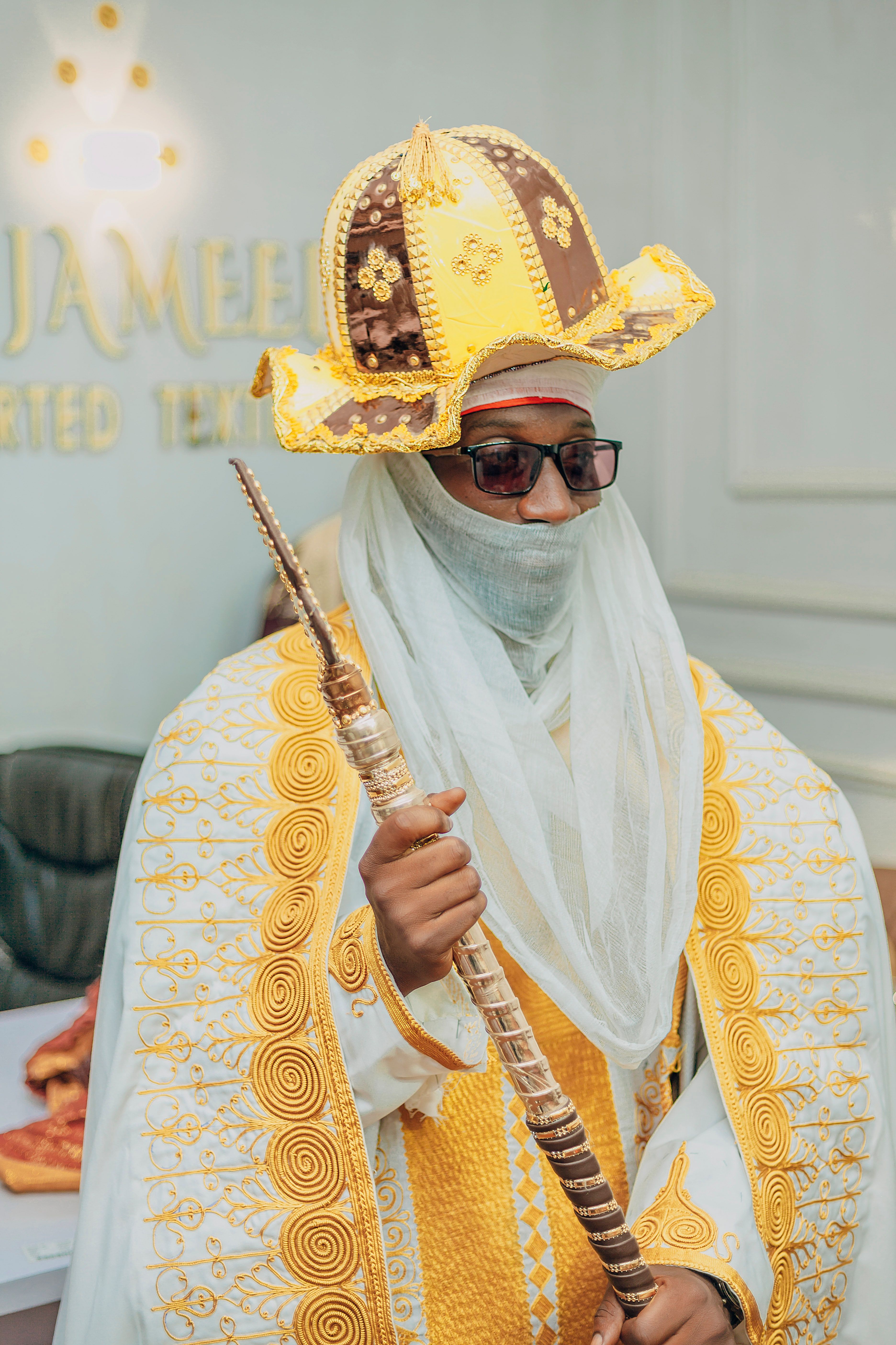 A person in elaborate yellow and brown traditional attire holding a staff, exuding a regal presence.
