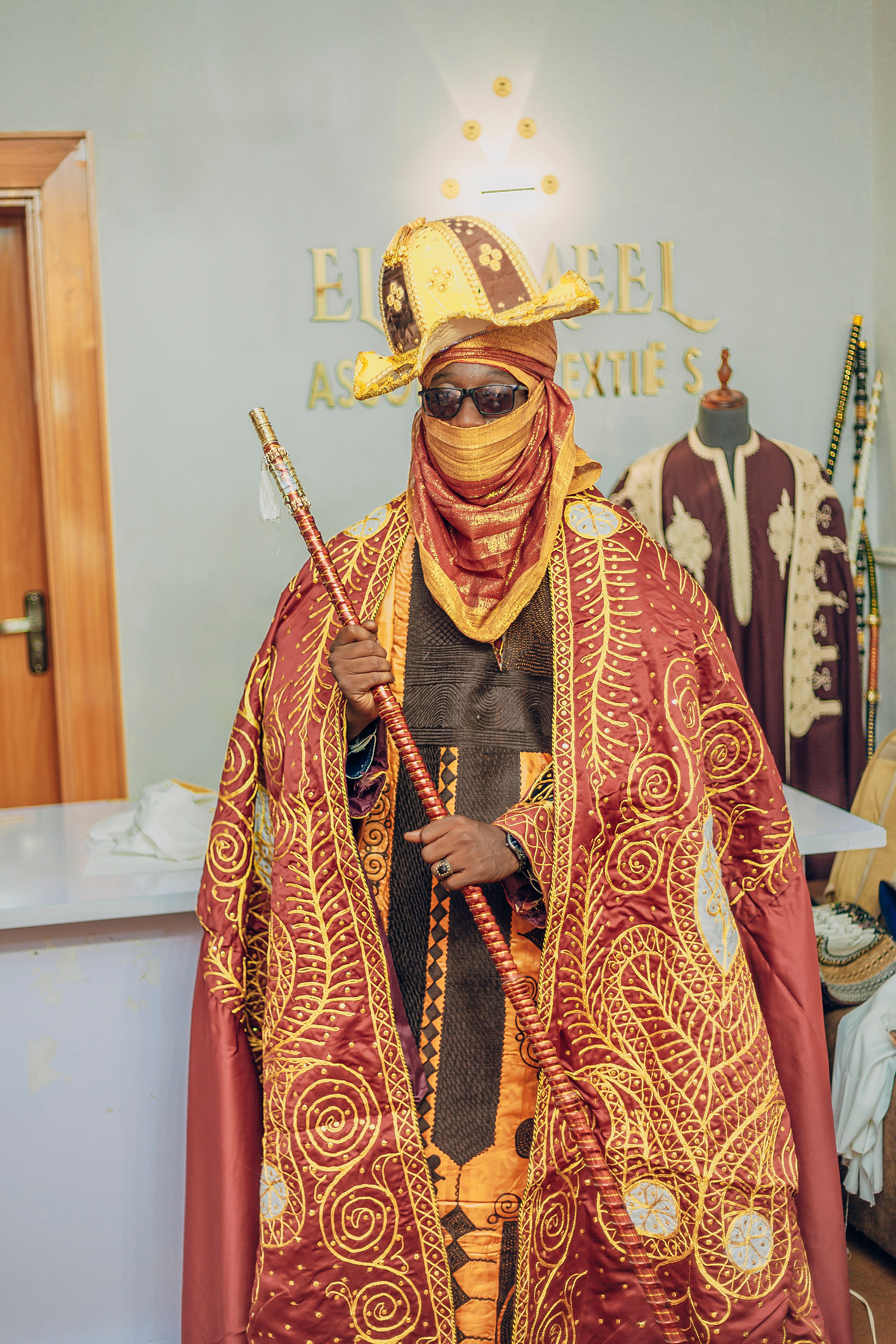 A person in elaborate traditional African attire with intricate patterns in a textile store.