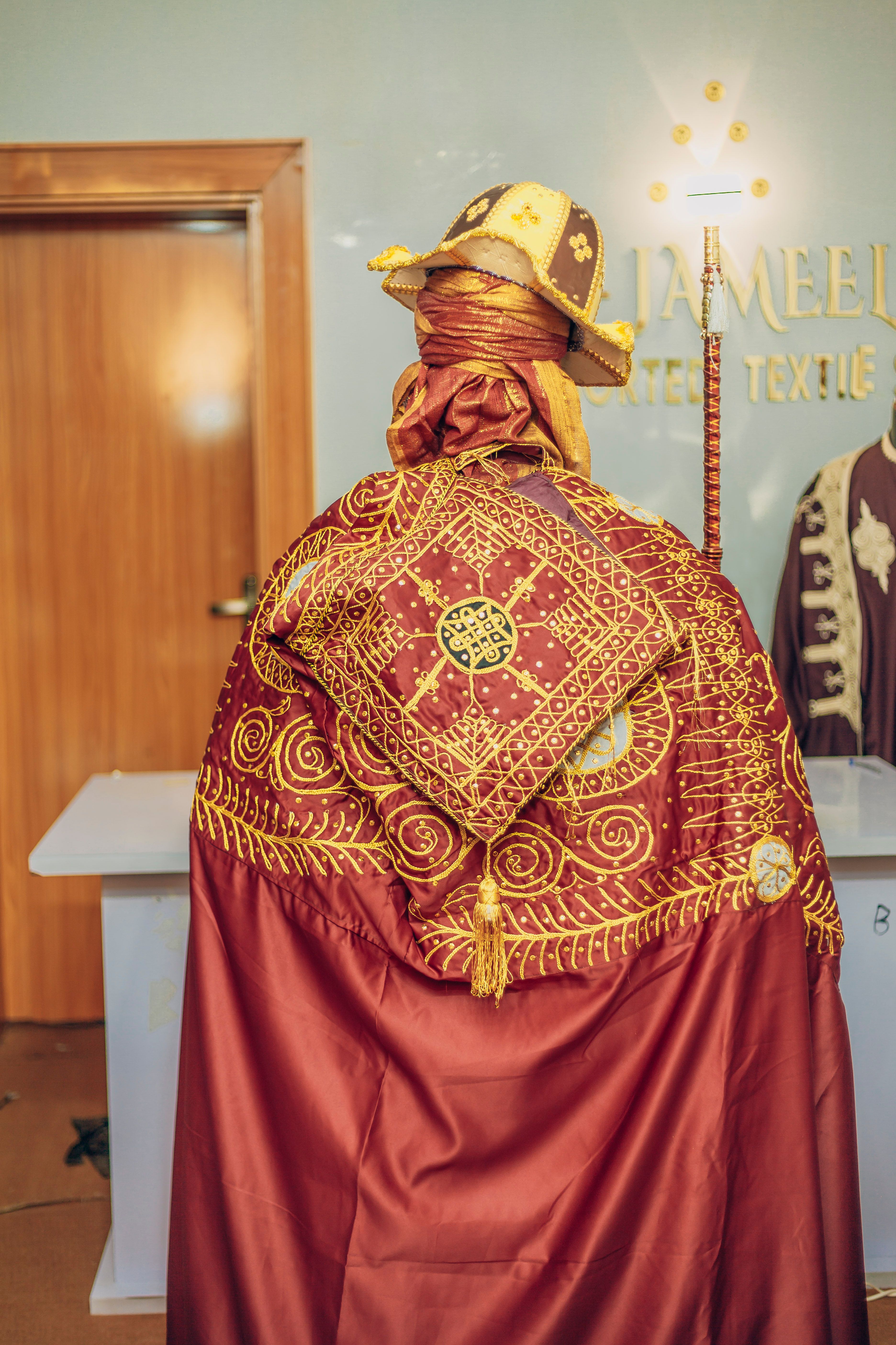 A person wearing ornate traditional African attire inside a textile showroom.