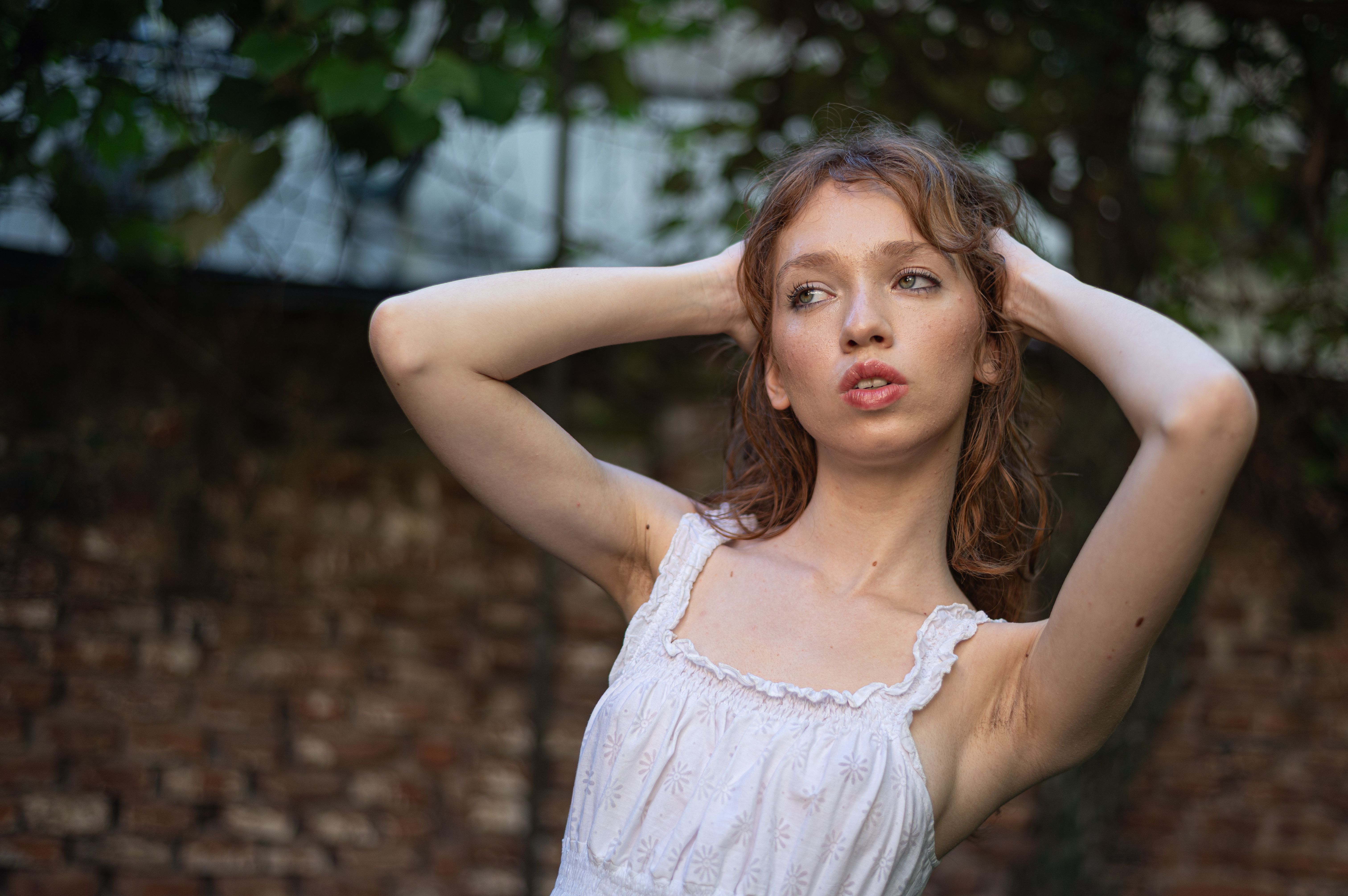 A woman in a white dress confidently poses outdoors, framed by greenery and natural light.