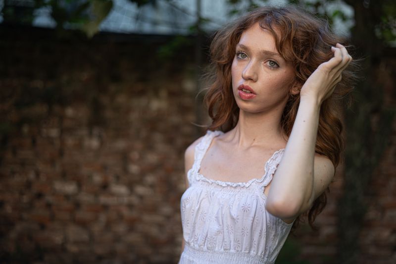 Close-up portrait of a young woman with red hair in a white dress outdoors.