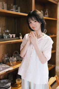 Young woman standing in a cozy kitchen with shelves filled with glassware.
