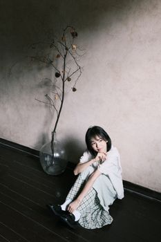 Young woman sitting indoors in a minimalist setting with subtle light.