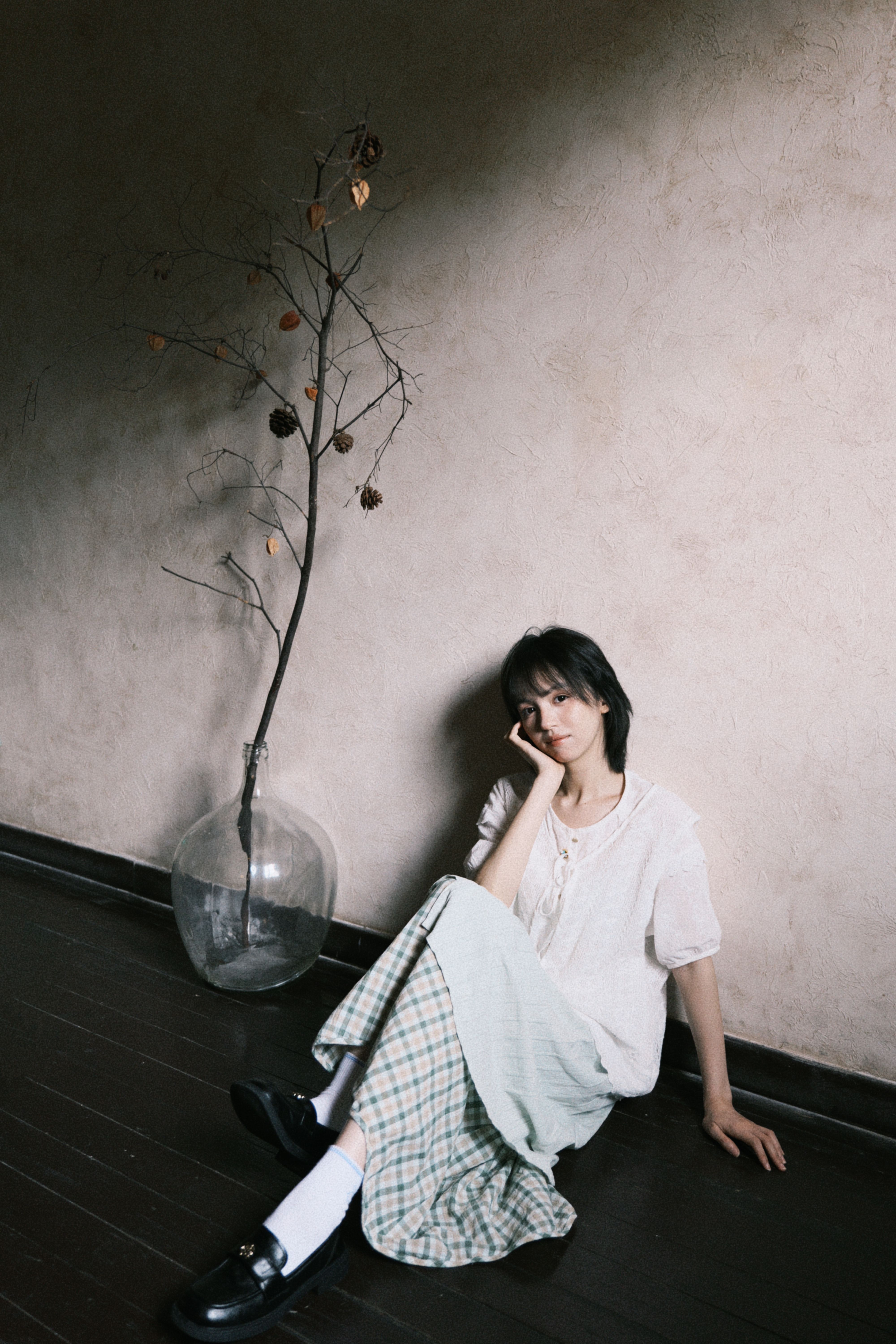 Woman in casual attire sitting indoors with minimalistic decor, evoking a serene and contemplative mood.