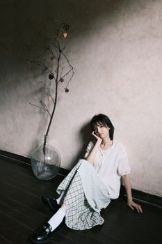Woman in casual attire sitting indoors with minimalistic decor, evoking a serene and contemplative mood.