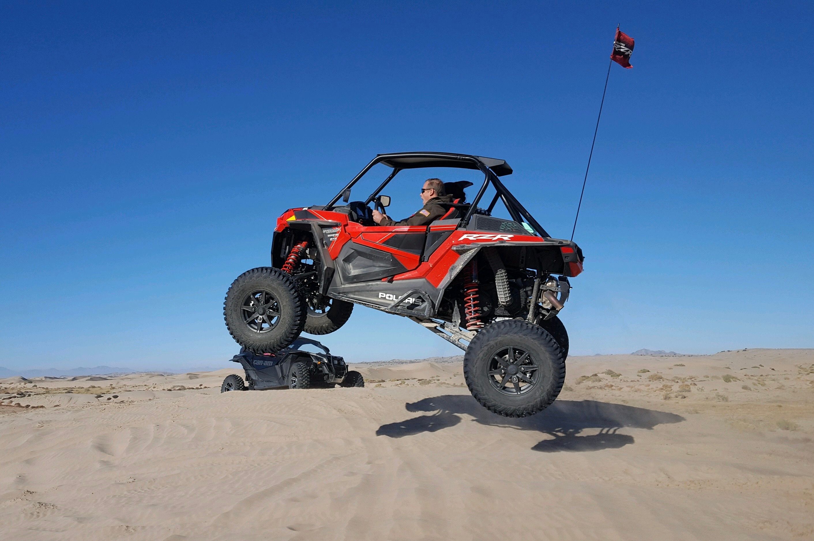 ATV catching air over a desert dune under a clear blue sky, thrilling adventure captured.