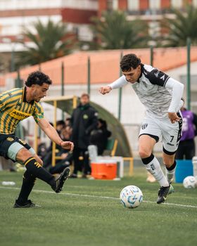Two soccer players in action during an outdoor match on a grassy field with spectators.