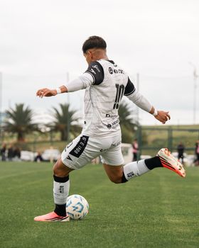 Athlete in action wearing white jersey, performing soccer kick on grass field.