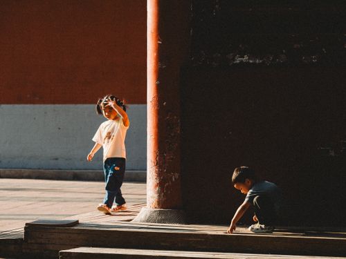 Free Two children playing in a sunlit courtyard with traditional architecture. Stock Photo